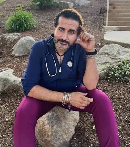 Dr. Nader Abdallah, DO, in navy scrubs with a stethoscope, seated outdoors